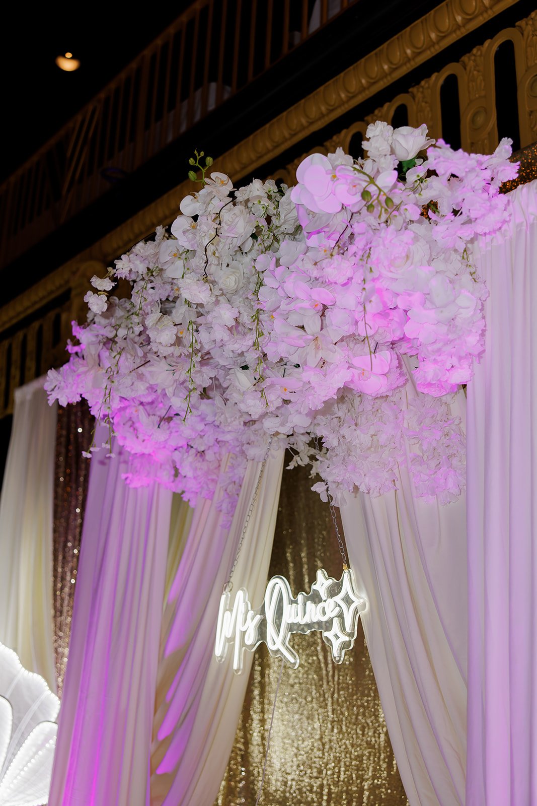 Detalle de un arreglo floral blanco y rosa sobre cortinas suaves en una quinceañera en Omaha