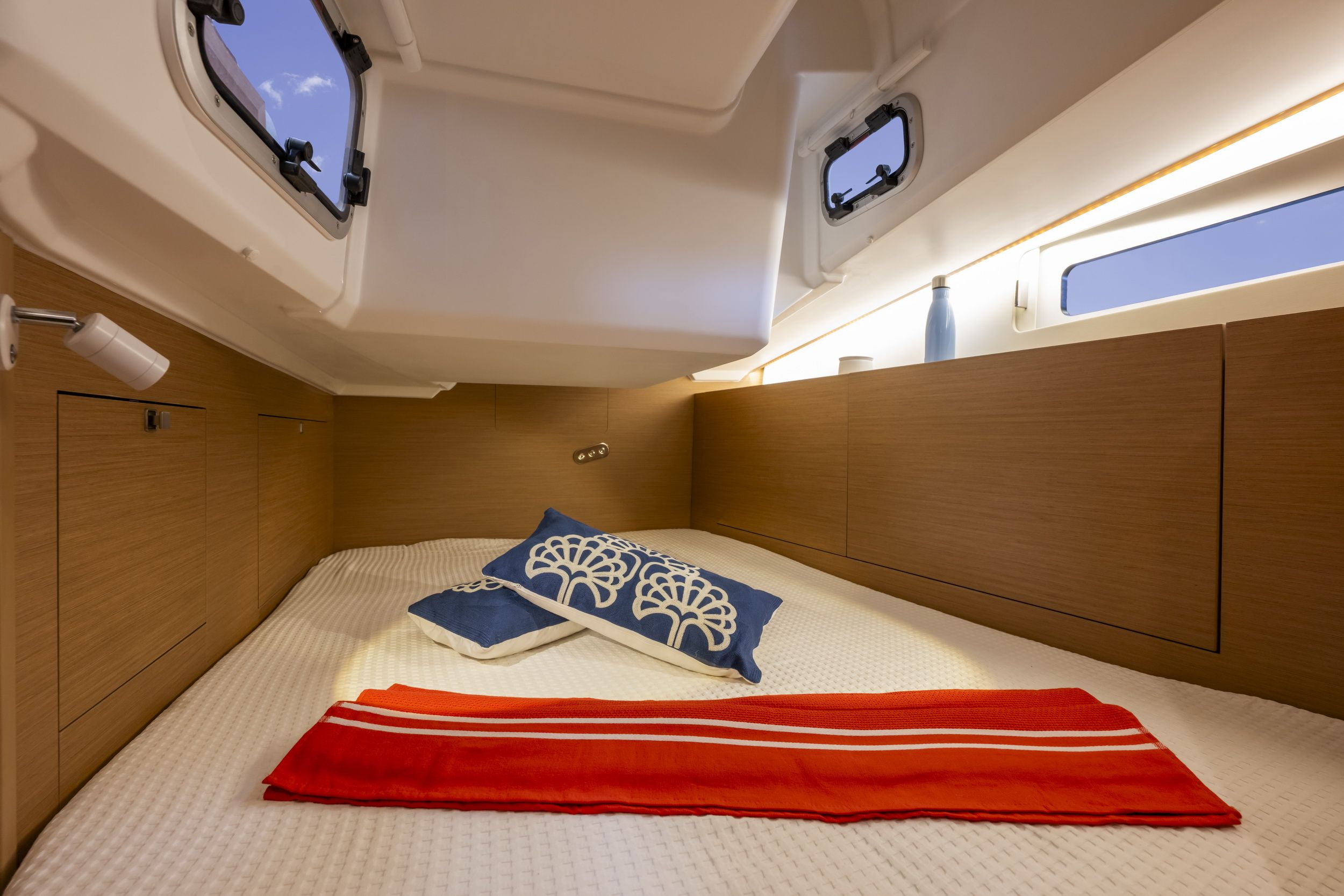 Wnętrze kabiny sypialnej jachtu Jeanneau Sun Odyssey 415 z dużym łóżkiem, poduszkami, kocem, oknami i szafkami.