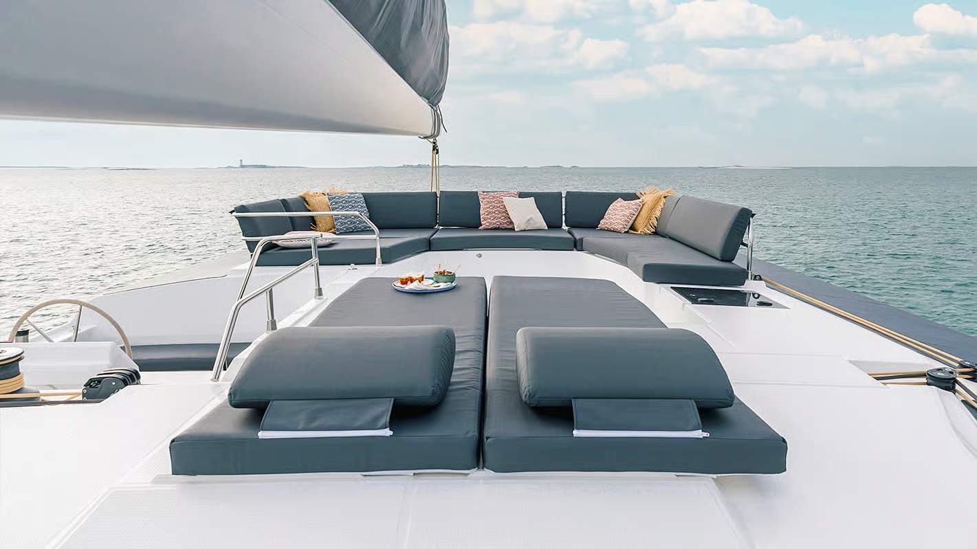 Widok na przestronny pokład dziobowy katamaranu Fountaine Pajot Aura 51 z wygodnymi leżakami i sofą.