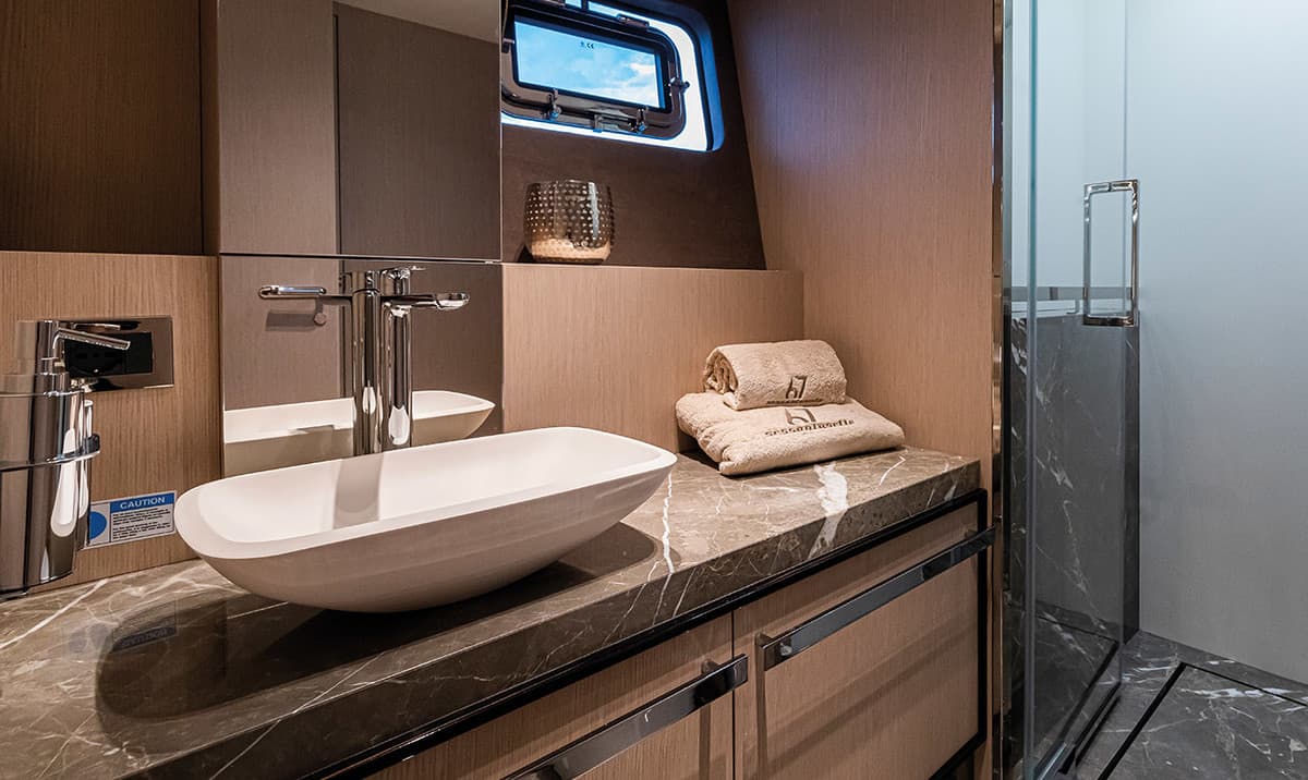 Basin with tap, mirror and porthole in a bathroom aboard the Cranchi Sessantasette 67. Towels and a shower cubicle alongside.