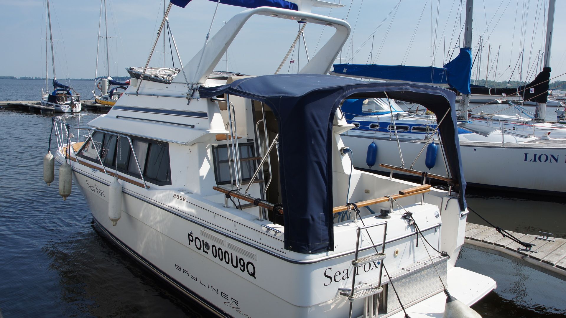 Motorówka Bayliner 2858 Classic Fly zacumowana w marinie, widok z rufy na flybridge z bimini i platformę kąpielową.