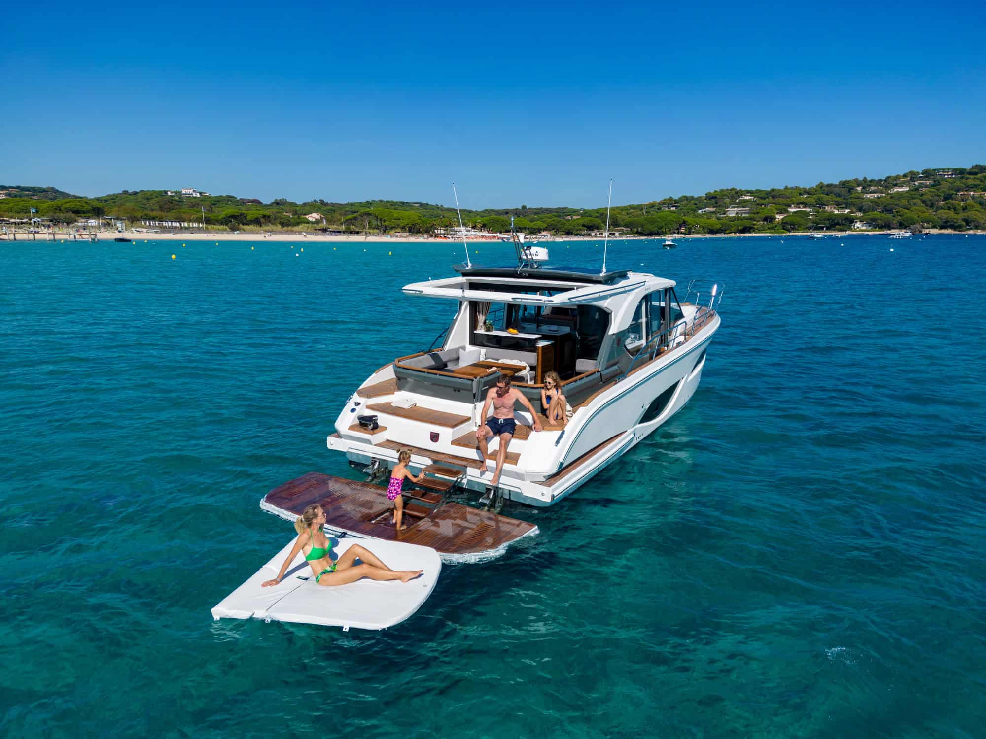 Marex 440 Gourmet Cruiser mit hydraulischer Badeplattform und Personen, die sich in einer Bucht entspannen. Im Hintergrund ein Sandstrand.