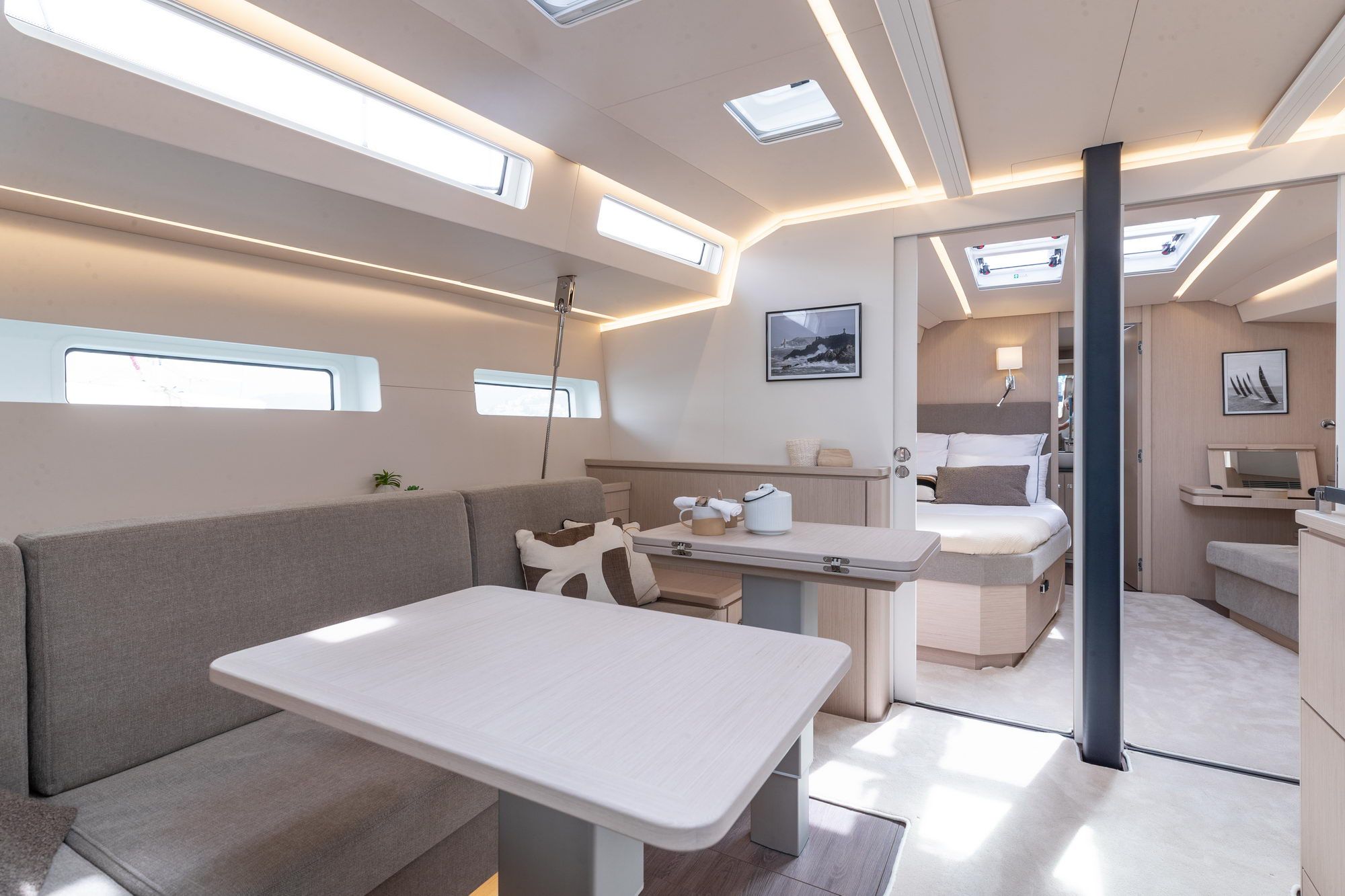 Innenraum der Jeanneau Yachts 55. Sichtbar sind der Salon mit Essbereich und die offene Eignerkabine mit Bett.