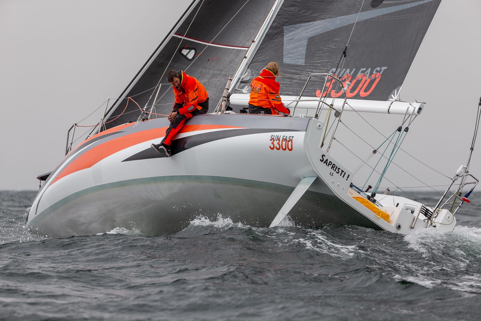Regattayacht Jeanneau Sun Fast 3300 mit zwei Seglern an der Reling, auf bewegtem Wasser während einer Regatta.