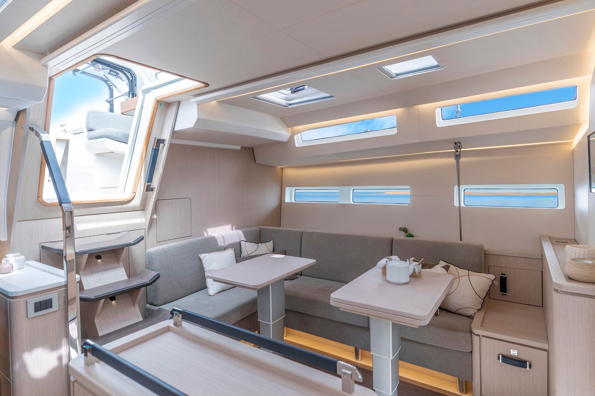 Salon-Innenraum der Segelyacht Jeanneau Yachts 55 mit Sitzbänken, Tischen und Blick auf das Cockpit durch den Niedergang.