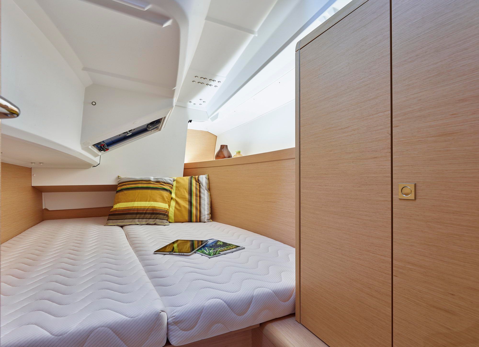 Wnętrze kabiny dziobowej jachtu żaglowego Jeanneau Sun Odyssey 349 z podwójnym łóżkiem i drewnianą szafką.