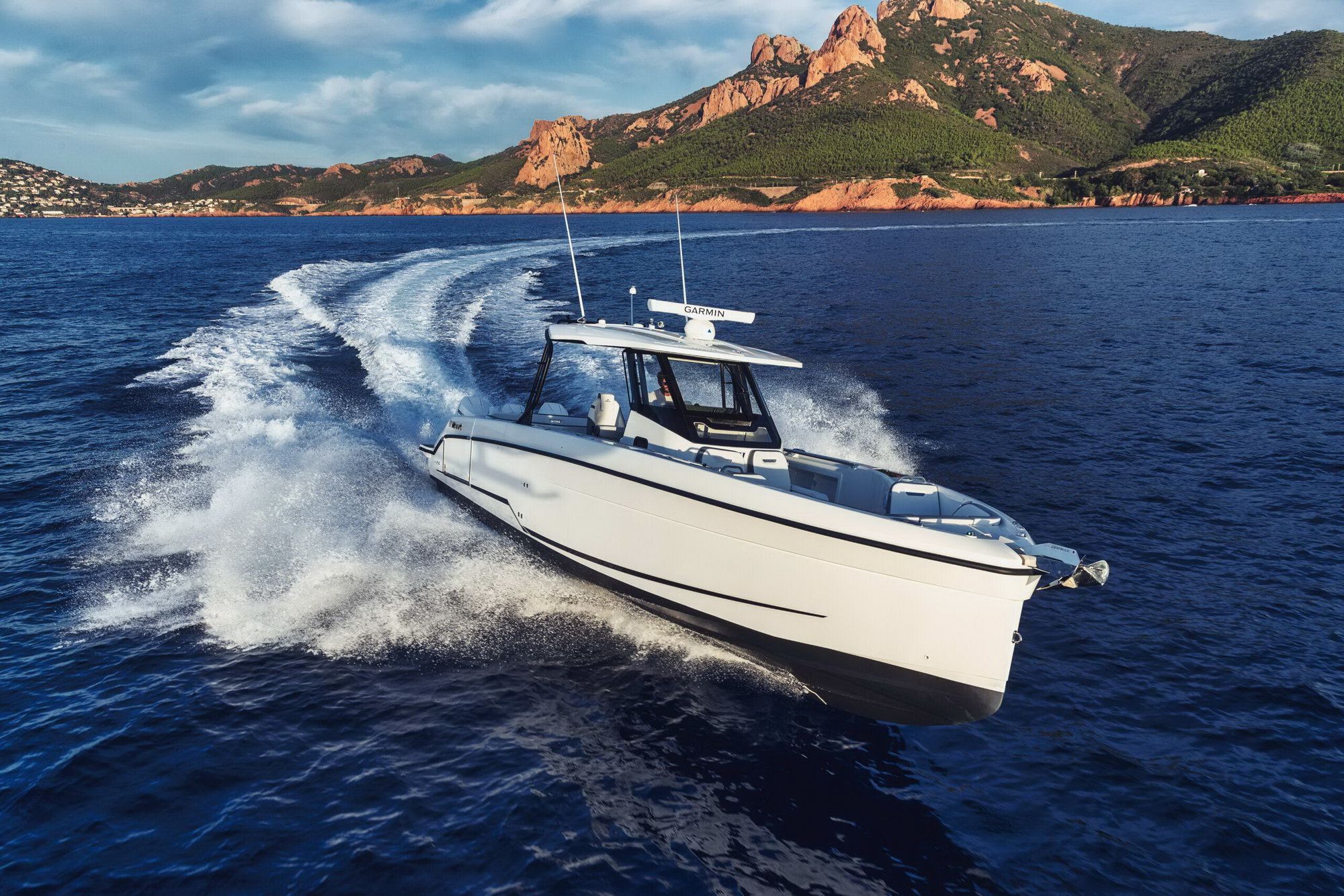Biała łódź motorowa Wellcraft 38 T-Top płynąca szybko po morzu, zostawiająca za sobą biały kilwater. W tle góry.