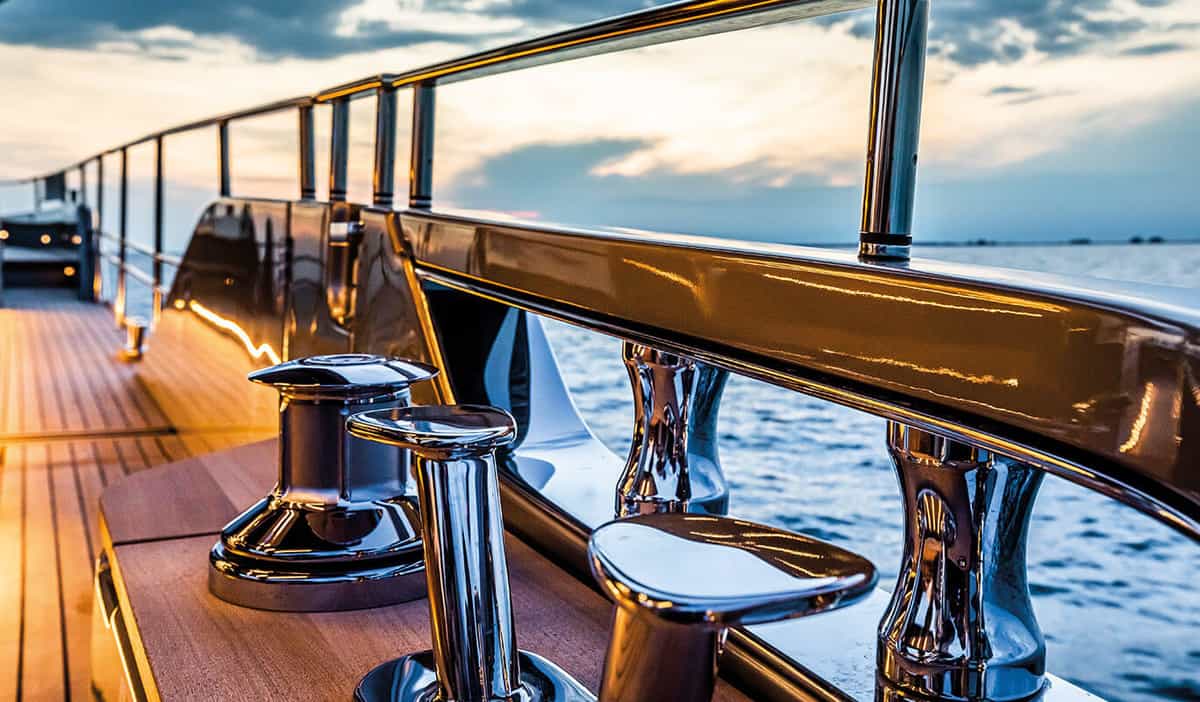 Chrome cleats and railings on the wooden deck of the Cranchi Sessantasette 67, with the sea at sunset in the background.