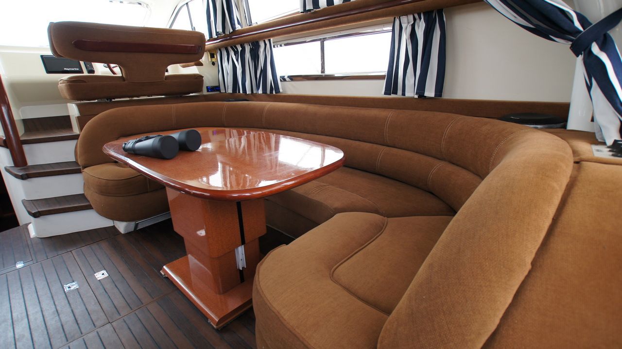Interior of the Sealine F44 Flybridge with brown sofa, wooden table and binoculars. Part of the helm station visible.
