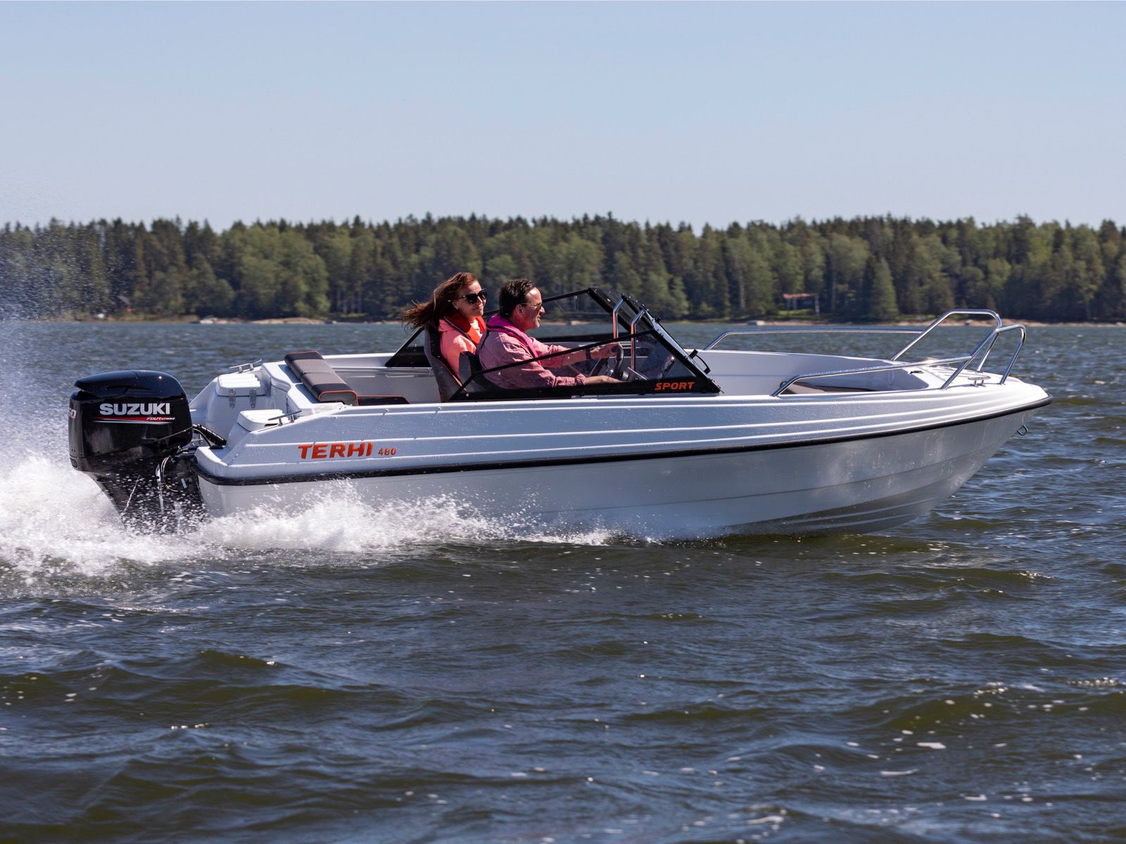 Biała łódź motorowa Terhi 480 Sport z silnikiem Suzuki płynąca po jeziorze z dwiema osobami na pokładzie.