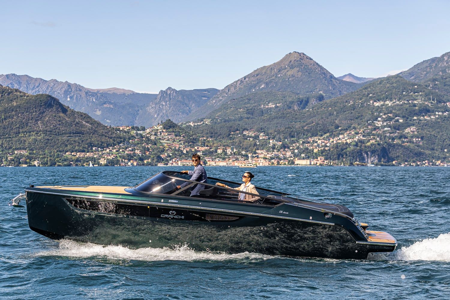 Cranchi E26 Classic Azzurro Infinito, a motor yacht underway on a lake with mountains in the background. Two people on board.