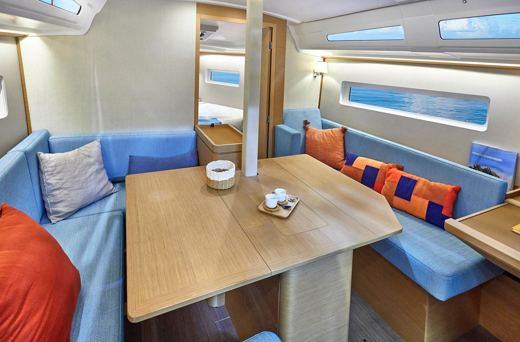 Heller Salon der Segelyacht Jeanneau Sun Odyssey 380 mit Holztisch, blauen Sofas und Meerblick.