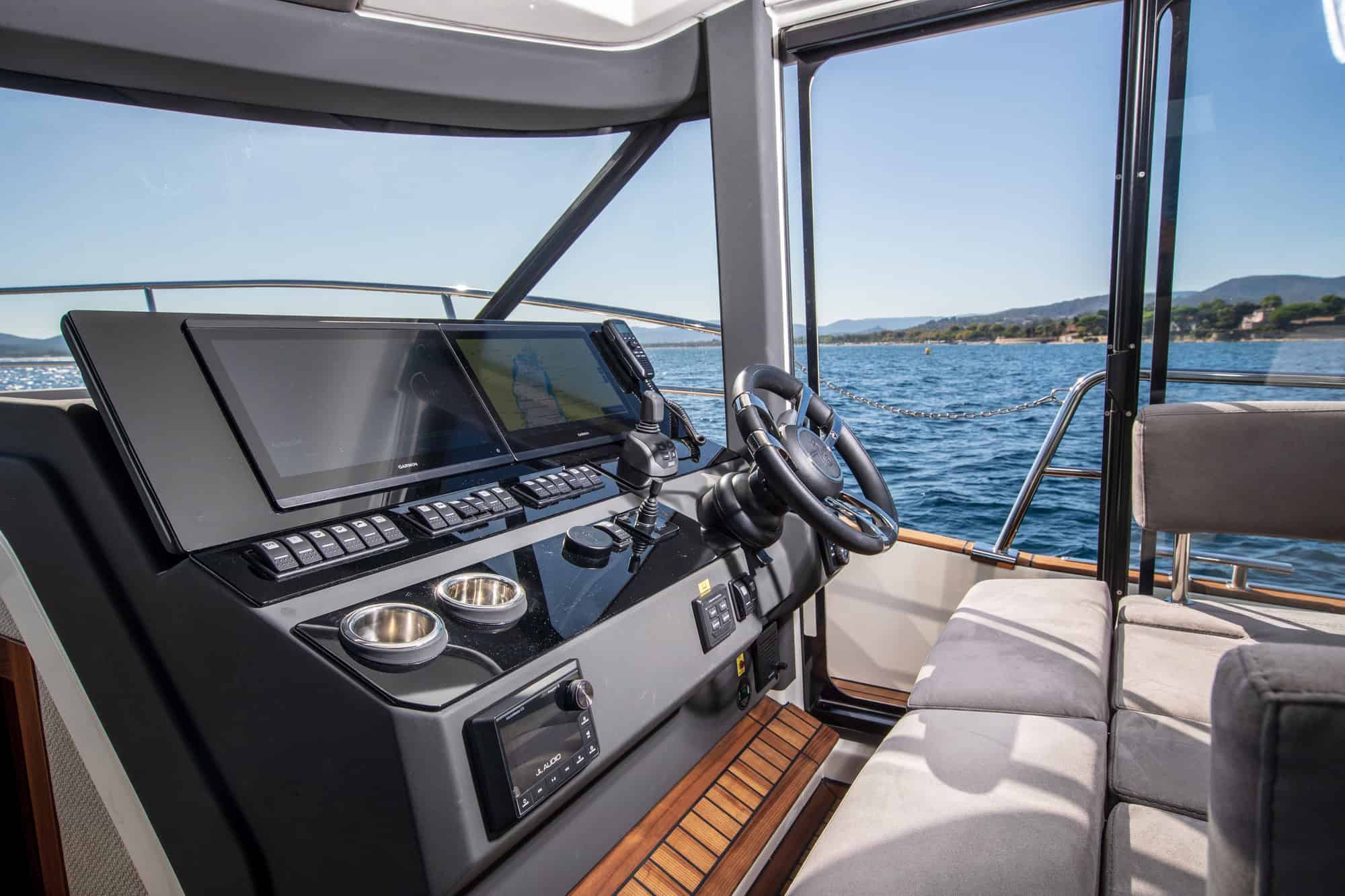 Wnętrze jachtu Marex 440 Gourmet Cruiser, widok na stanowisko sternika z kierownicą, ekranami nawigacyjnymi i panelem sterowania.
