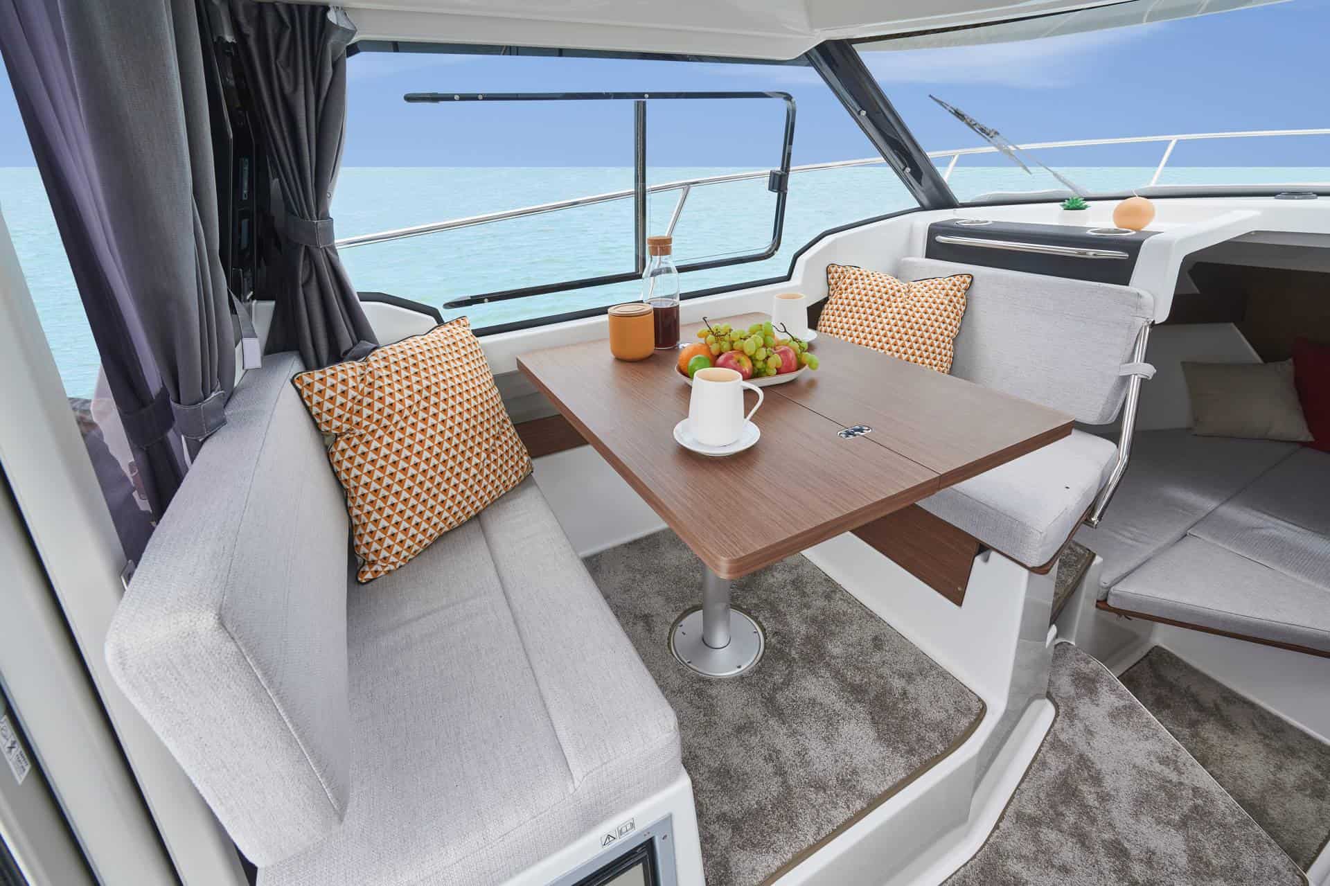 Innenansicht der Motoryacht Jeanneau Merry Fisher 795 mit Holztisch, Sofas und Meerblick.