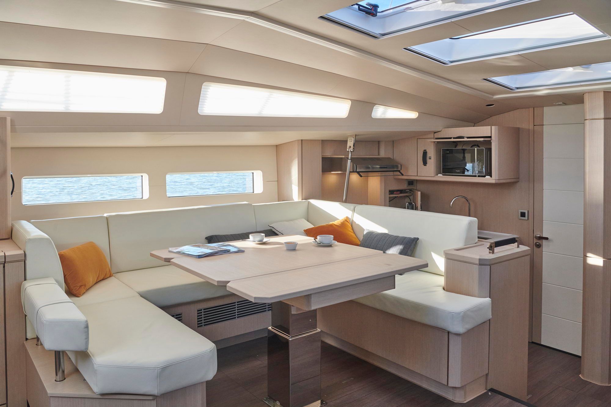 Interior of the Jeanneau Yachts 60 with the saloon, fold-out table, U-shaped sofa and part of the galley.