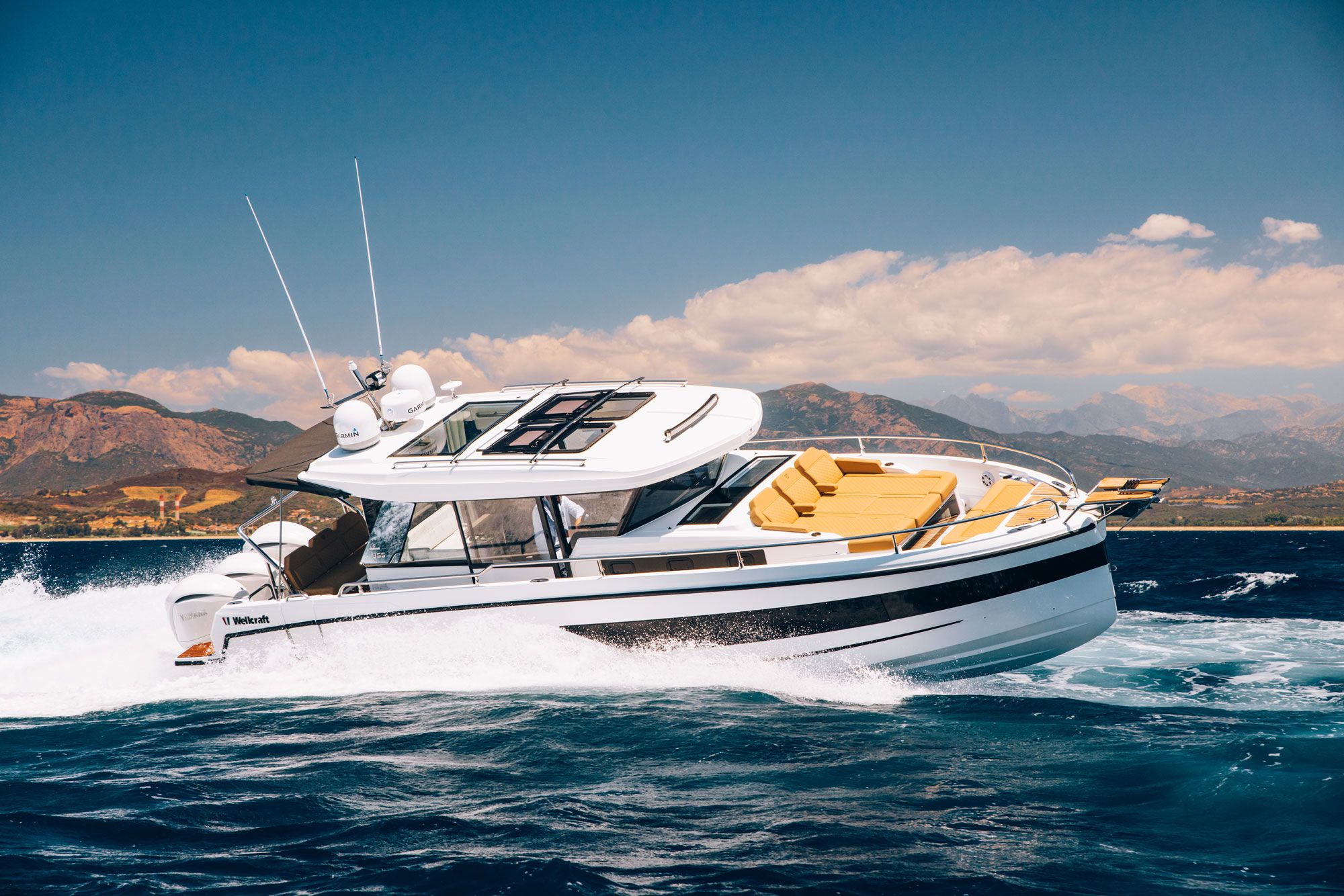Wellcraft 38 Explorer, biało-czarny jacht motorowy, płynący po morzu, z górami w tle.
