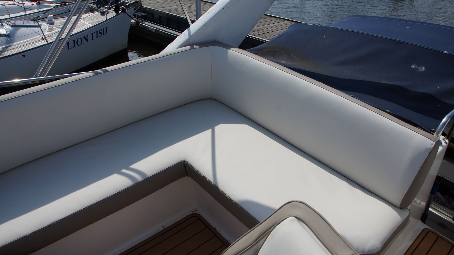 Neues helles L-förmiges Polster auf der Flybridge der Bayliner 2858 Classic Fly. Im Hintergrund sind ein Teil einer anderen Yacht und Wasser zu sehen.