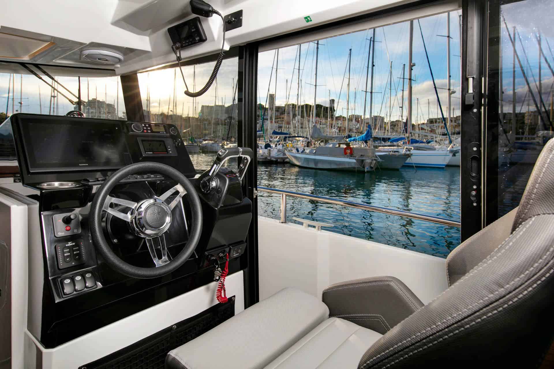 Interior of the Jeanneau Merry Fisher 895 Sport S2, the helm station with wheel, navigation display and a view of the marina.