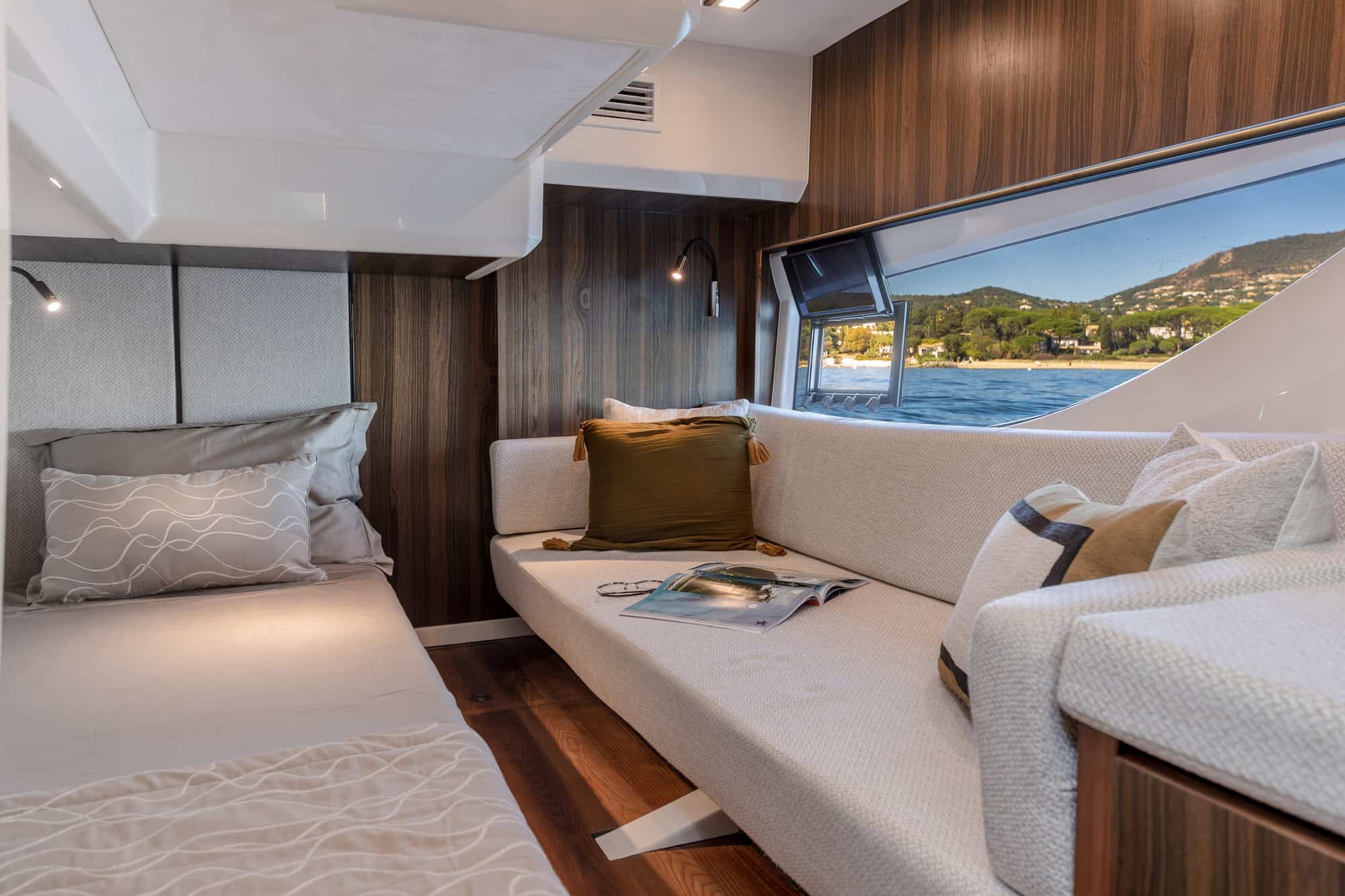 Interior of a cabin on the Marex 440 Gourmet Cruiser with bed, sofa and a large window with a view of the sea and coastline.