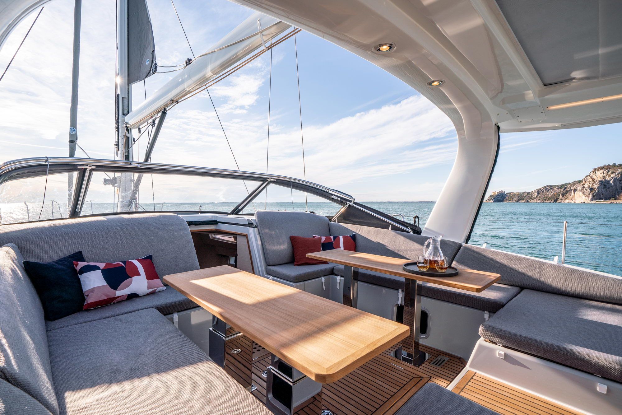 Blick auf das geräumige Cockpit der Jeanneau Yachts 65 mit bequemen Sitzbänken, Holztischen und Meerblick.