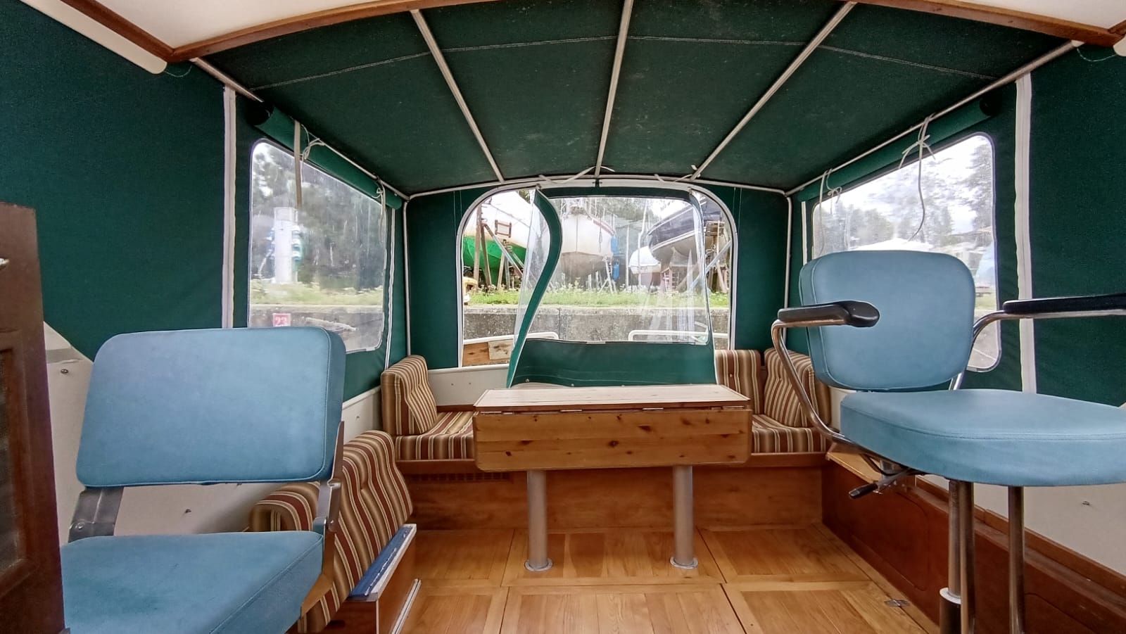 Cockpit-Innenraum der Aquanaut 750 mit grünem Cabrio-Verdeck, zwei Sitzen und einem Holztisch.