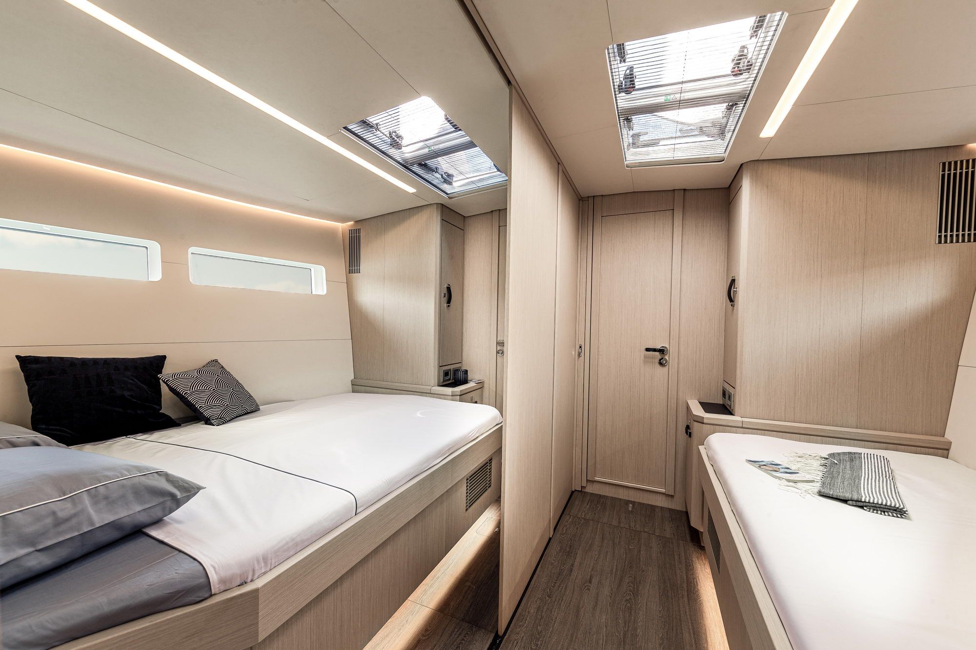 Wnętrze kabiny gościnnej na jachcie Jeanneau Yachts 60 z dwoma pojedynczymi łóżkami, jasnym drewnem i świetlikami.