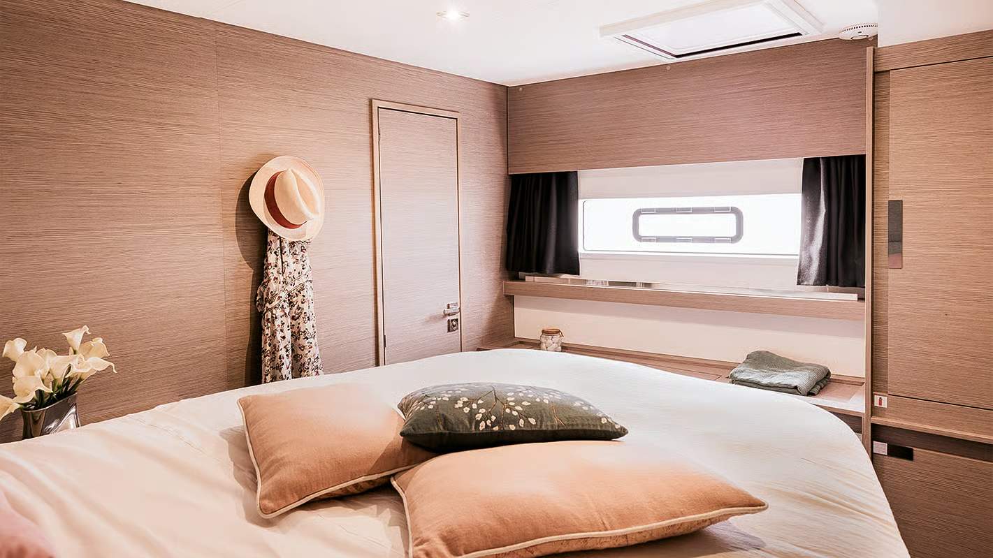 Wnętrze kabiny sypialnej na katamaranie Fountaine Pajot Aura 51 z dużym łóżkiem, oknem i drewnianymi panelami ściennymi.