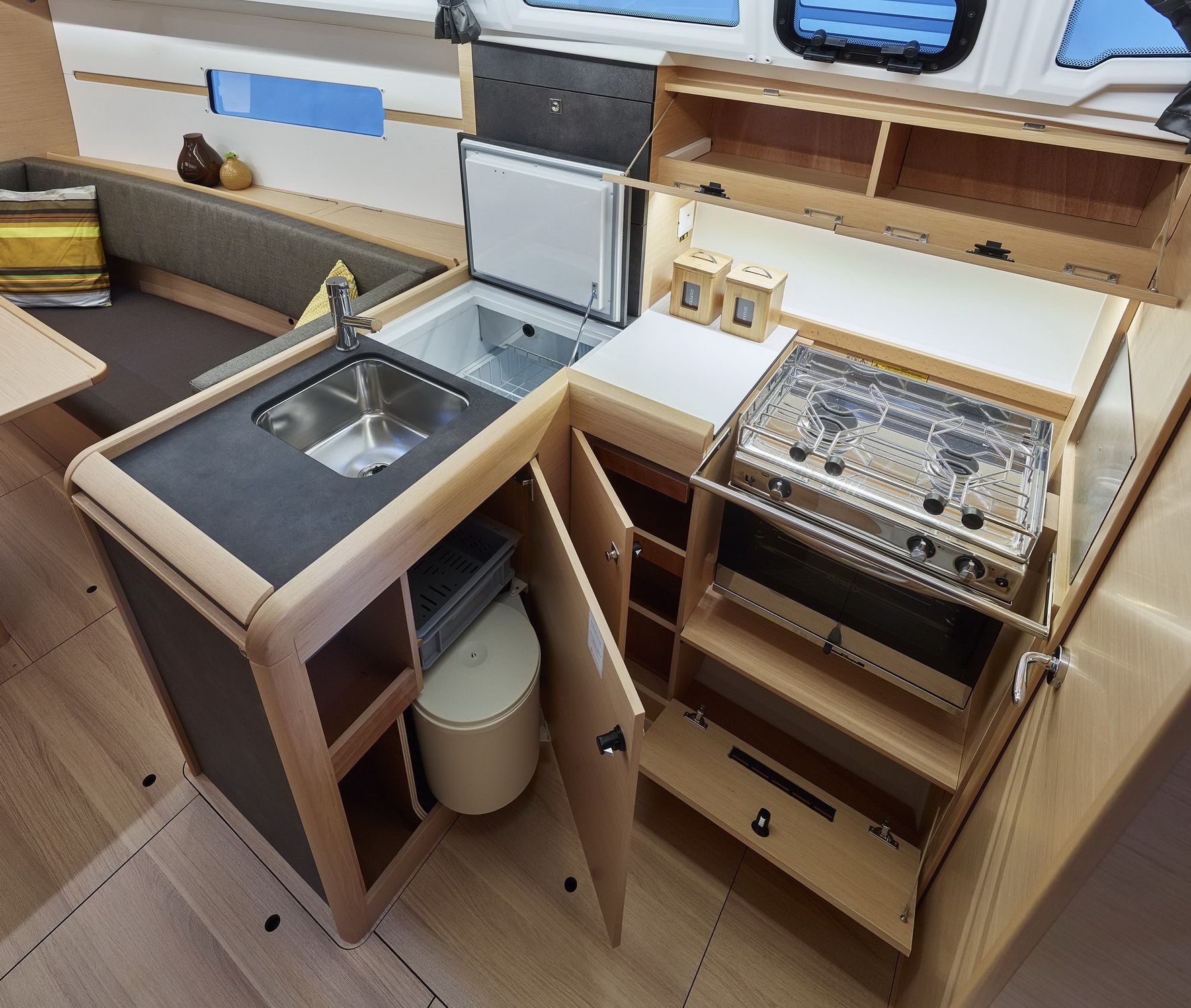 Wnętrze jachtu Jeanneau Sun Odyssey 349, przedstawiające w pełni wyposażony kambuz z lodówką, zlewem, kuchenką i piekarnikiem.