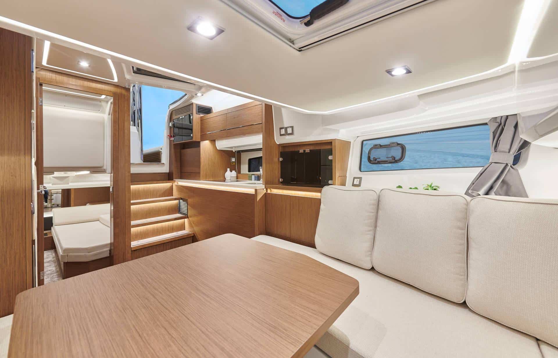 View of the interior of the Jeanneau Cap Camarat 12.5 WA, showing the saloon with sofa, table, galley and entrance to the sleeping cabin.