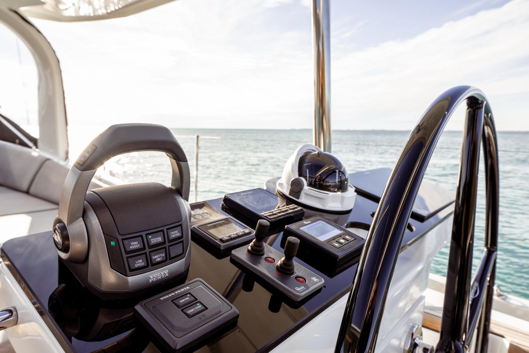Stanowisko sternika jachtu Jeanneau Yachts 65 z manetką Volvo Penta, joystickiem i kompasem, na tle morza.