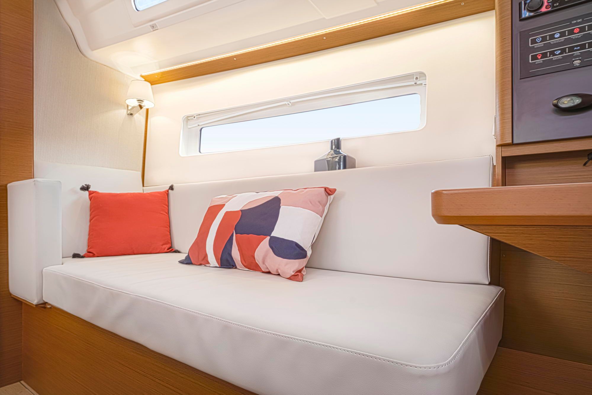 Jasne wnętrze jachtu Jeanneau Sun Odyssey 380 z białą kanapą, poduszkami, oknem i panelem sterowania.