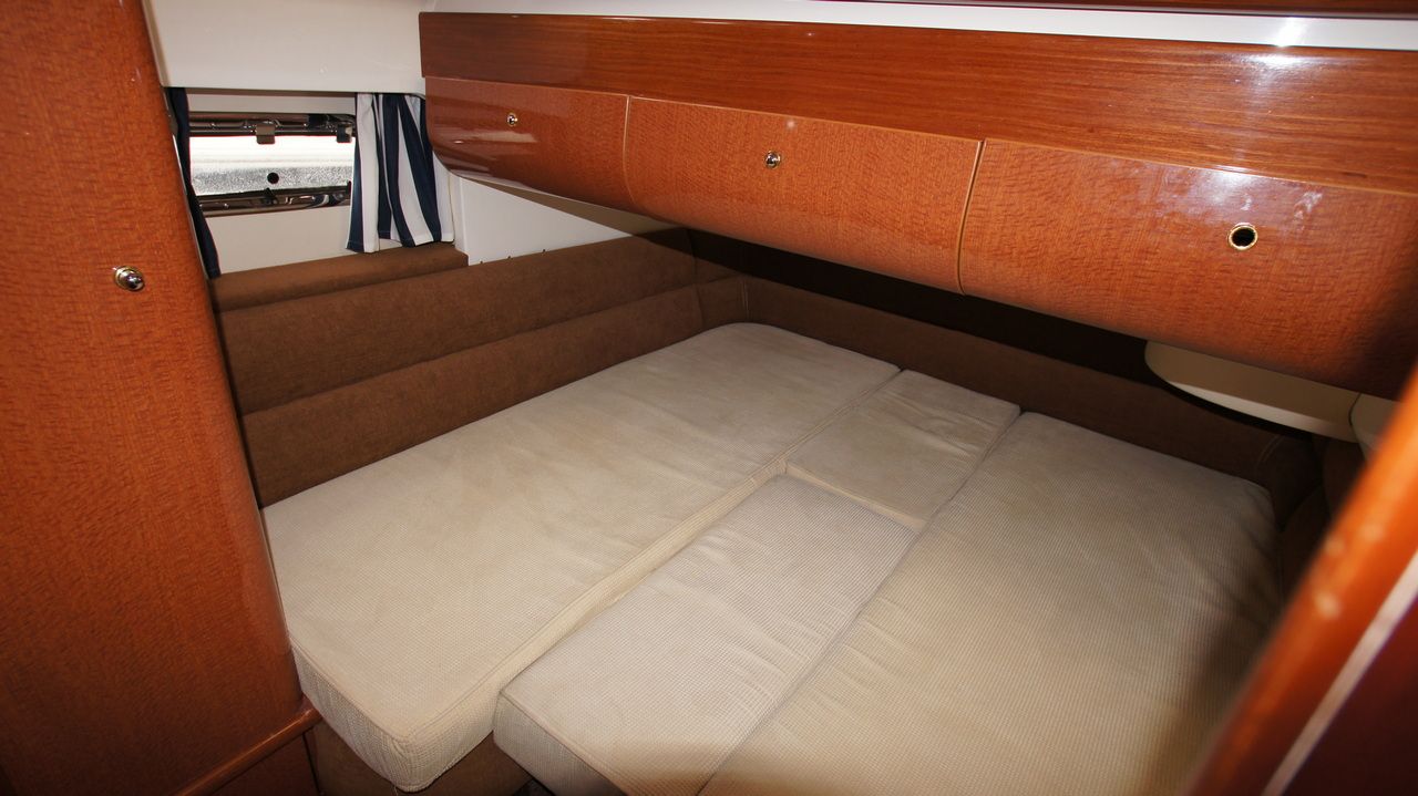 Wnętrze kabiny sypialnej na jachcie Sealine F44 Flybridge z łóżkiem i drewnianymi szafkami.