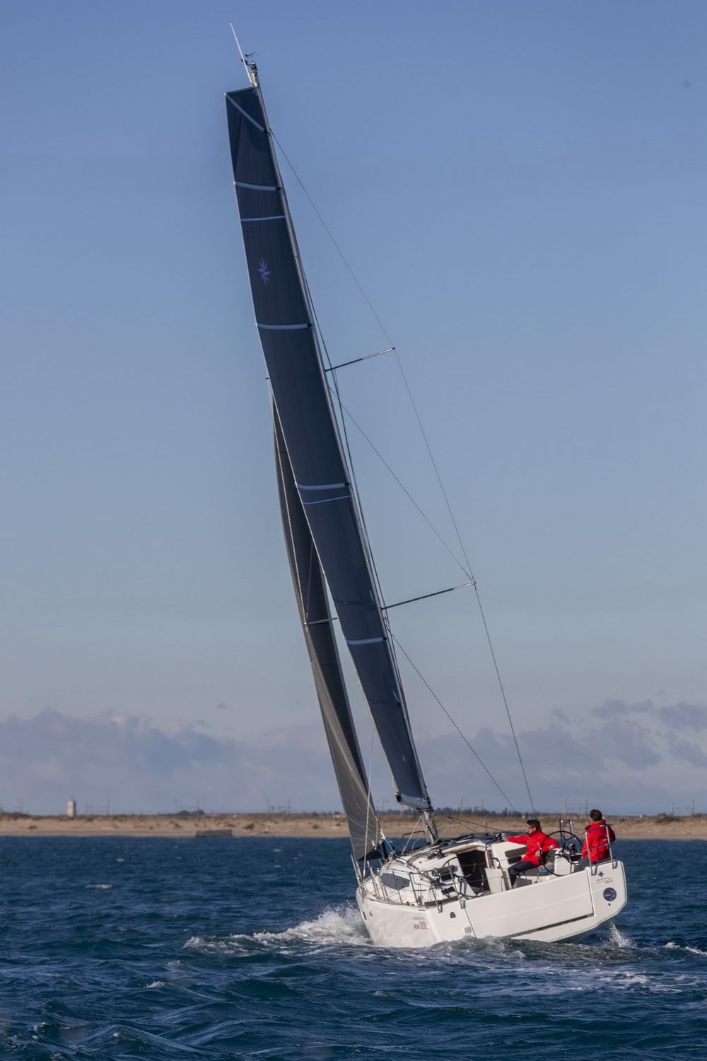 Jacht żaglowy Jeanneau Sun Odyssey 380 płynący pod żaglami na morzu, z dwoma osobami w kokpicie. Widoczny odwrócony dziób.