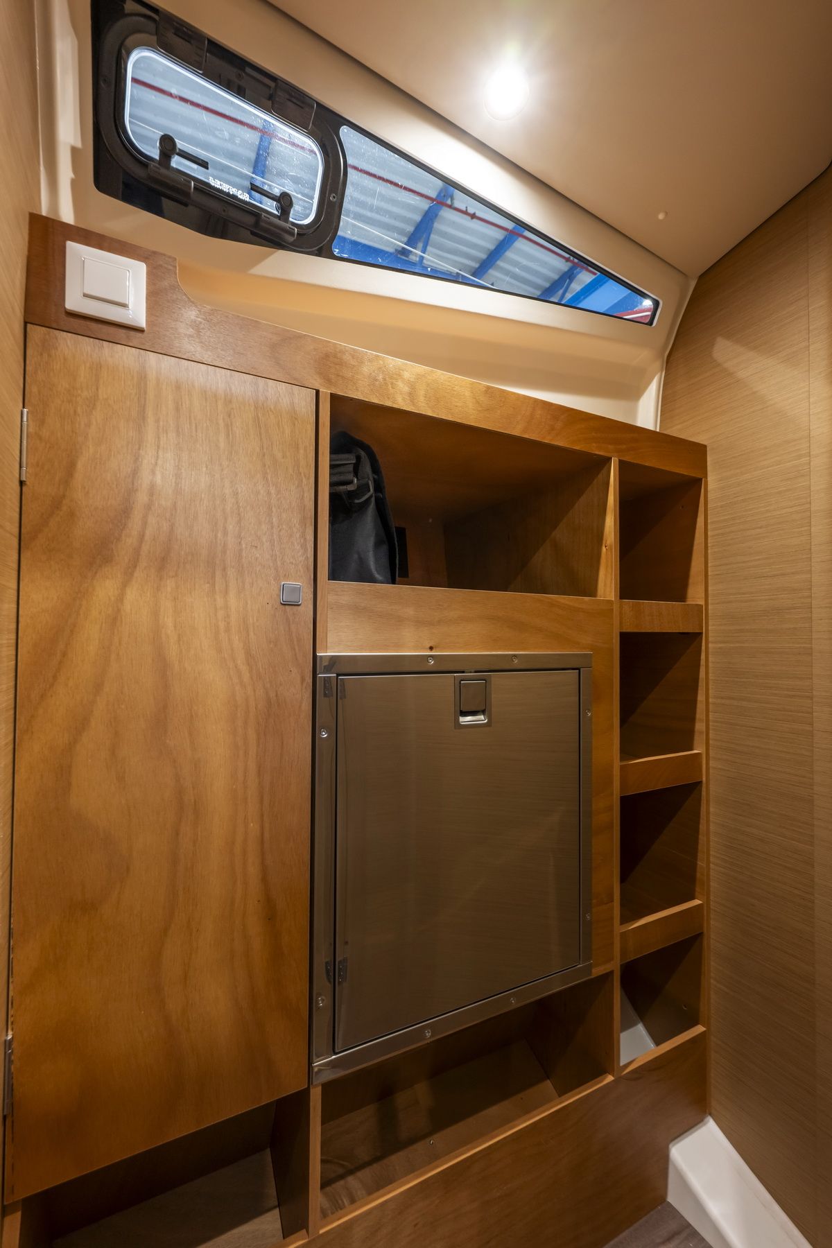 Innenraum einer Kabine der Jeanneau Sun Odyssey 455 mit Holzverkleidung, Kühlschrank und Rumpffenster.