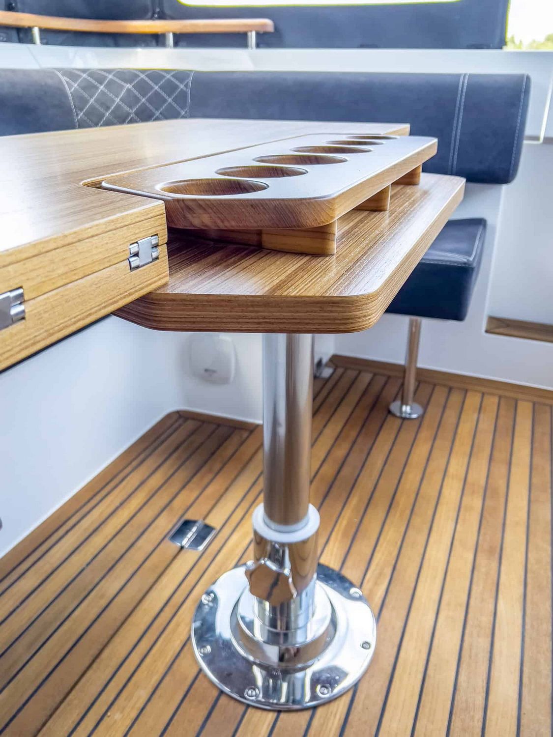 Holztisch mit Becherhaltern im Cockpit der Marex 310 Sun Cruiser, mit gepolsterten Sitzen und Holzboden.