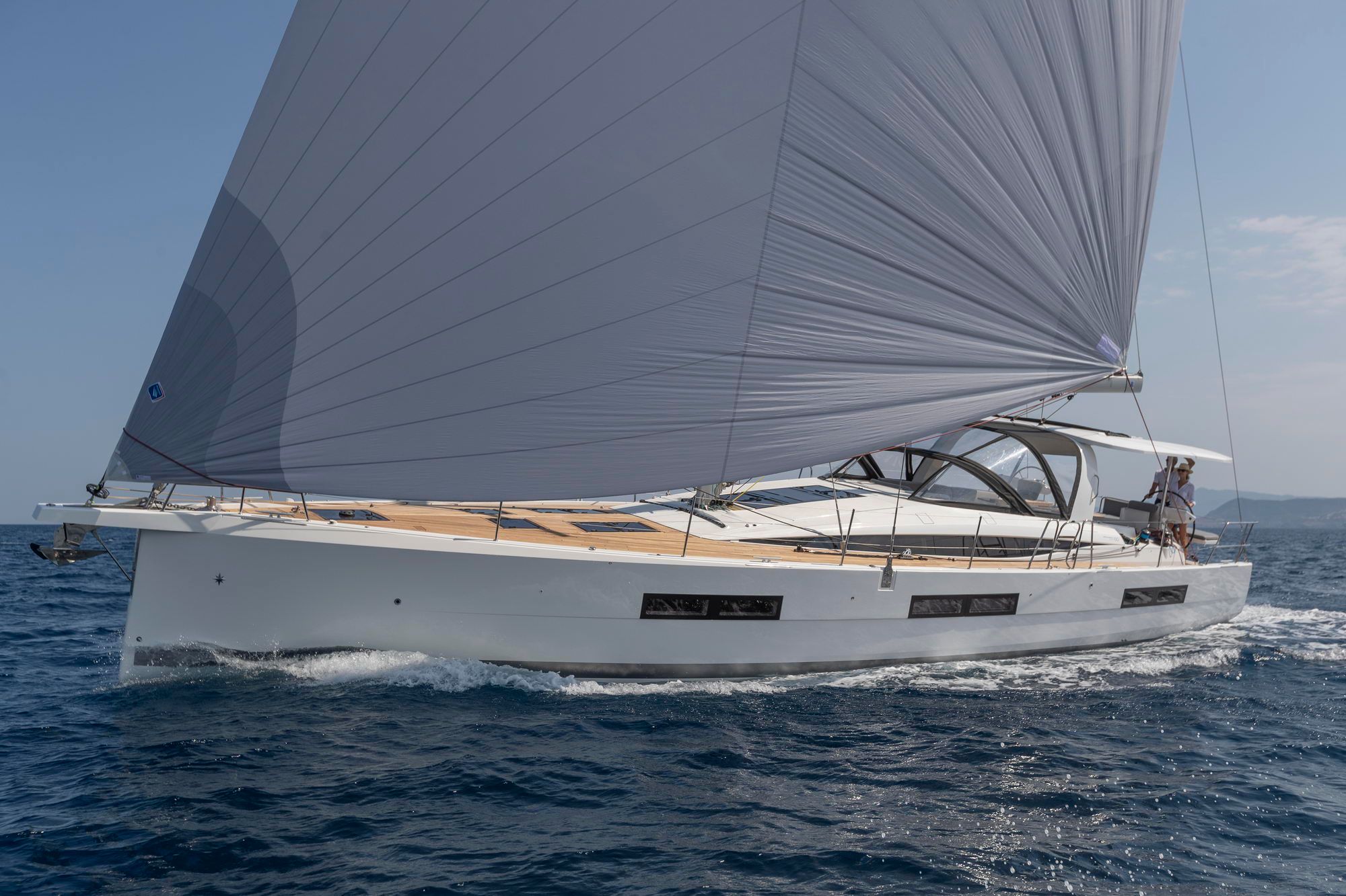 Biały jacht żaglowy Jeanneau Yachts 60 płynący po morzu z rozwiniętym żaglem przednim. Widoczny dziób i burta.