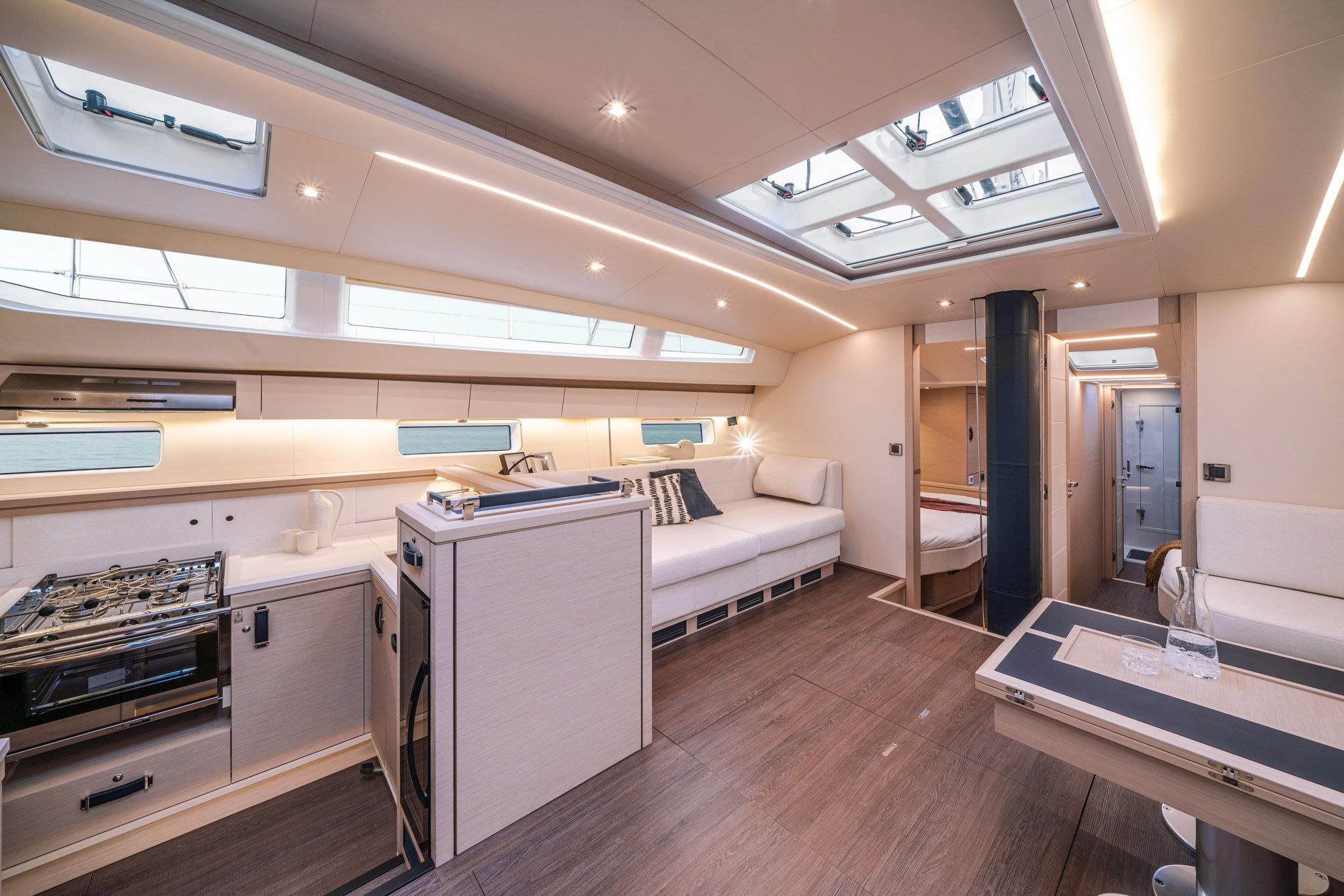 Jasne wnętrze jachtu Jeanneau Yachts 65 z kuchnią, salonem i widokiem na kabiny.