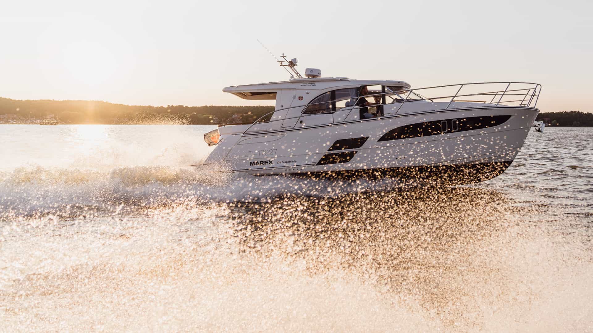 Biały jacht motorowy Marex 330 Scandinavia płynący szybko po wodzie, tworzący pianę, o zachodzie słońca.