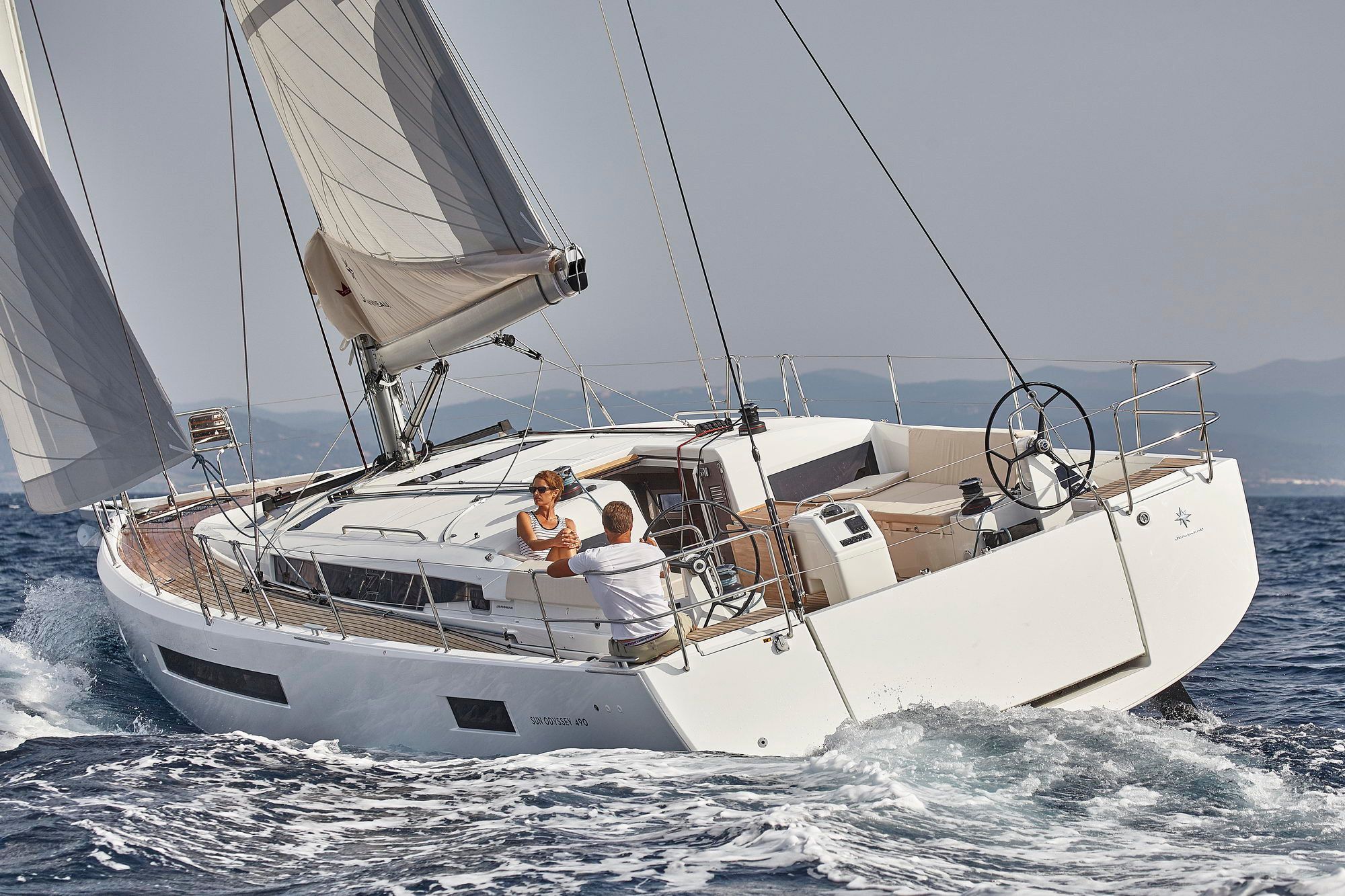 Biały jacht żaglowy Jeanneau Sun Odyssey 490 płynący po morzu z dwoma osobami w kokpicie, widok z boku.