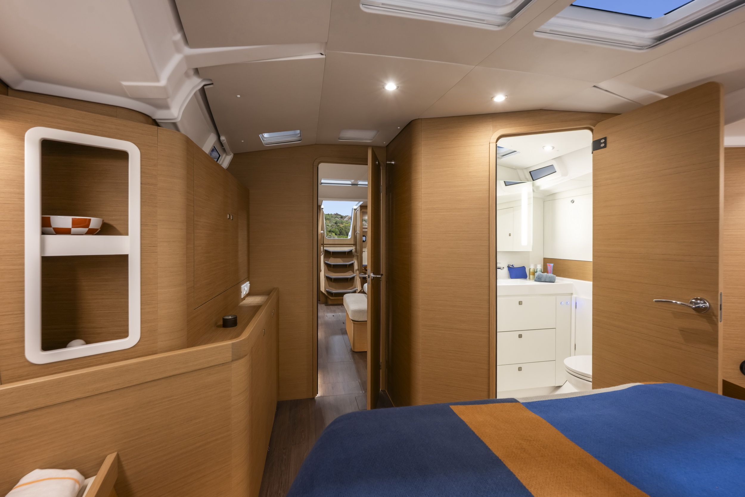 Wnętrze kabiny dziobowej jachtu Jeanneau Sun Odyssey 455 z łóżkiem, otwartą łazienką i przejściem do salonu.