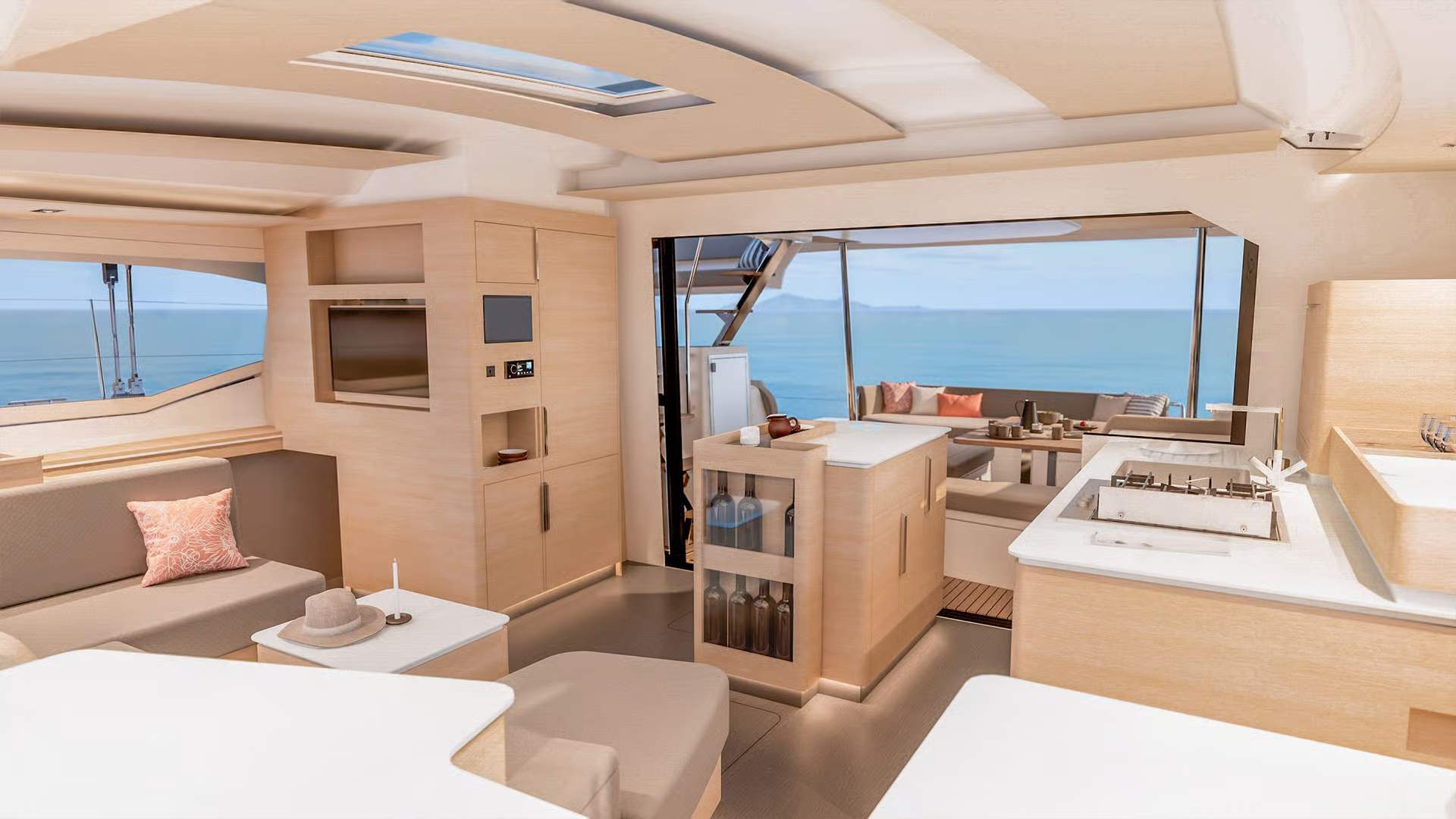 Przestronny salon katamaranu Fountaine Pajot FP48 z widokiem na otwarty kokpit rufowy i morze. Jasne drewno, nowoczesna kuchnia.