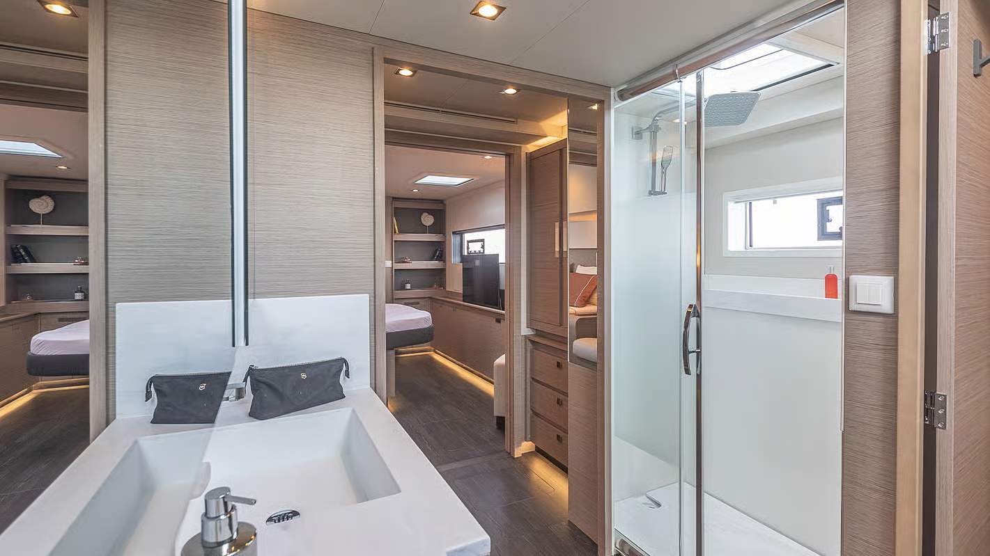 Wnętrze katamaranu Fountaine Pajot Samana 59 z widokiem na elegancką łazienkę z umywalką i prysznicem oraz przyległą kabinę.