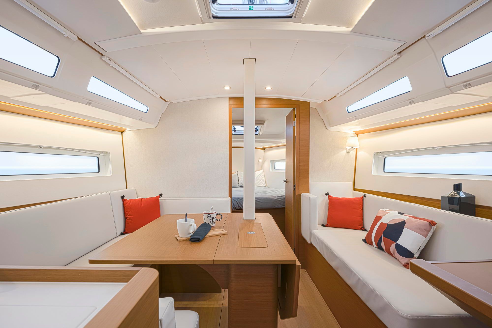 Jasne wnętrze salonu jachtu Jeanneau Sun Odyssey 380 z drewnianym stołem, białymi kanapami i oknami bocznymi.