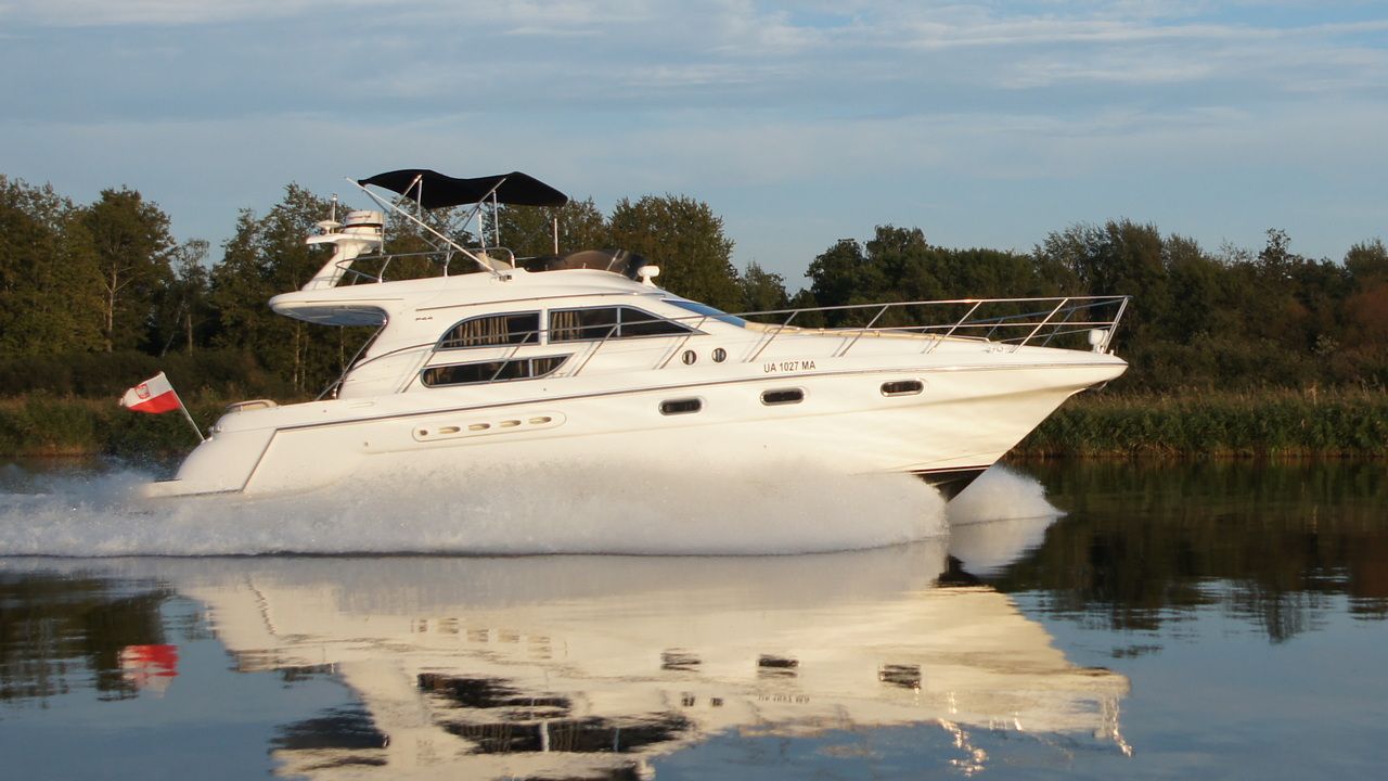 Biały jacht motorowy Sealine F44 Flybridge płynący po spokojnej wodzie, tworzący wyraźny kilwater. Widok z boku.