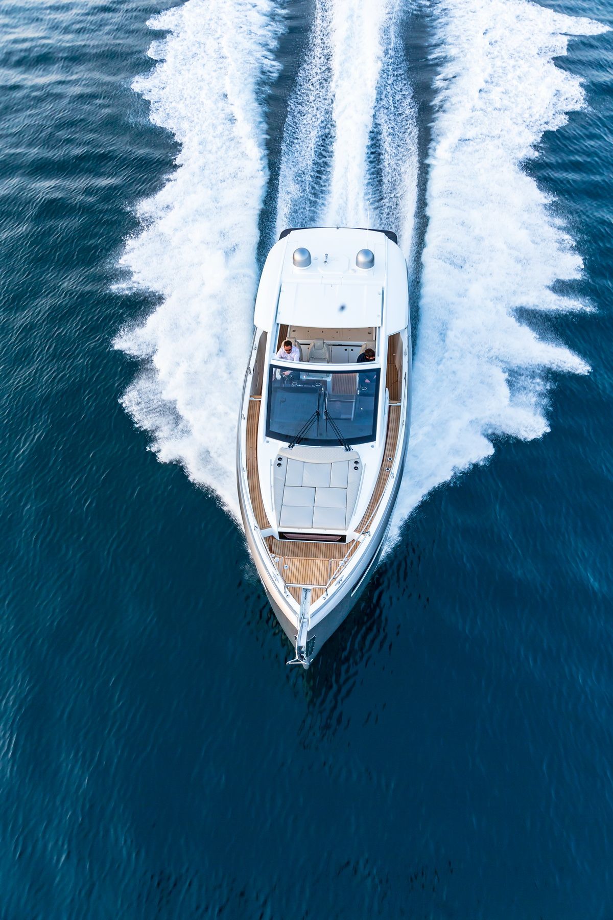 Luftaufnahme der Motoryacht Jeanneau DB/43 IB bei schneller Fahrt, mit weißem Kielwasser. Bugdeck und Cockpit mit zwei Personen sind sichtbar.