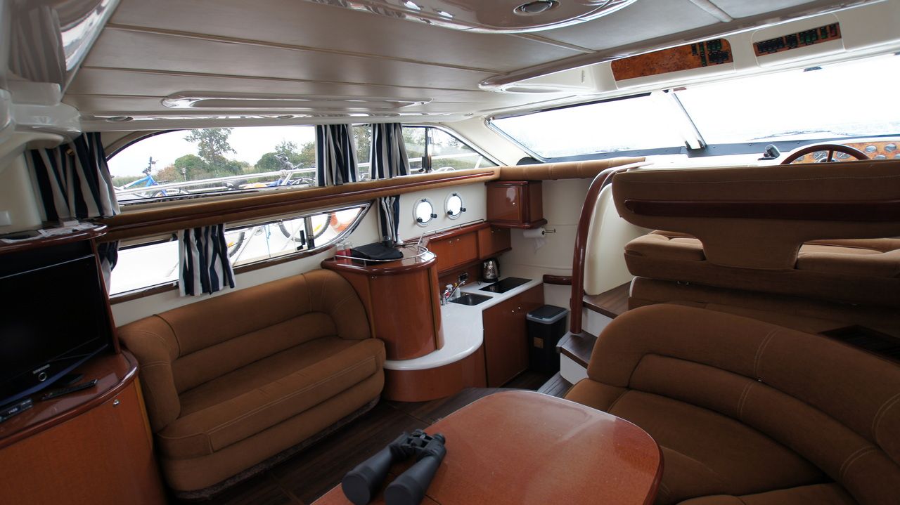 Wnętrze jachtu Sealine F44 Flybridge, przestronny salon z sofami, aneksem kuchennym i widoczną sterówką.