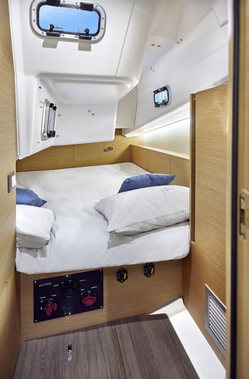 Wnętrze kabiny dziobowej jachtu Sun Odyssey 380 z prostokątną koją, oknami i panelem akumulatorów.