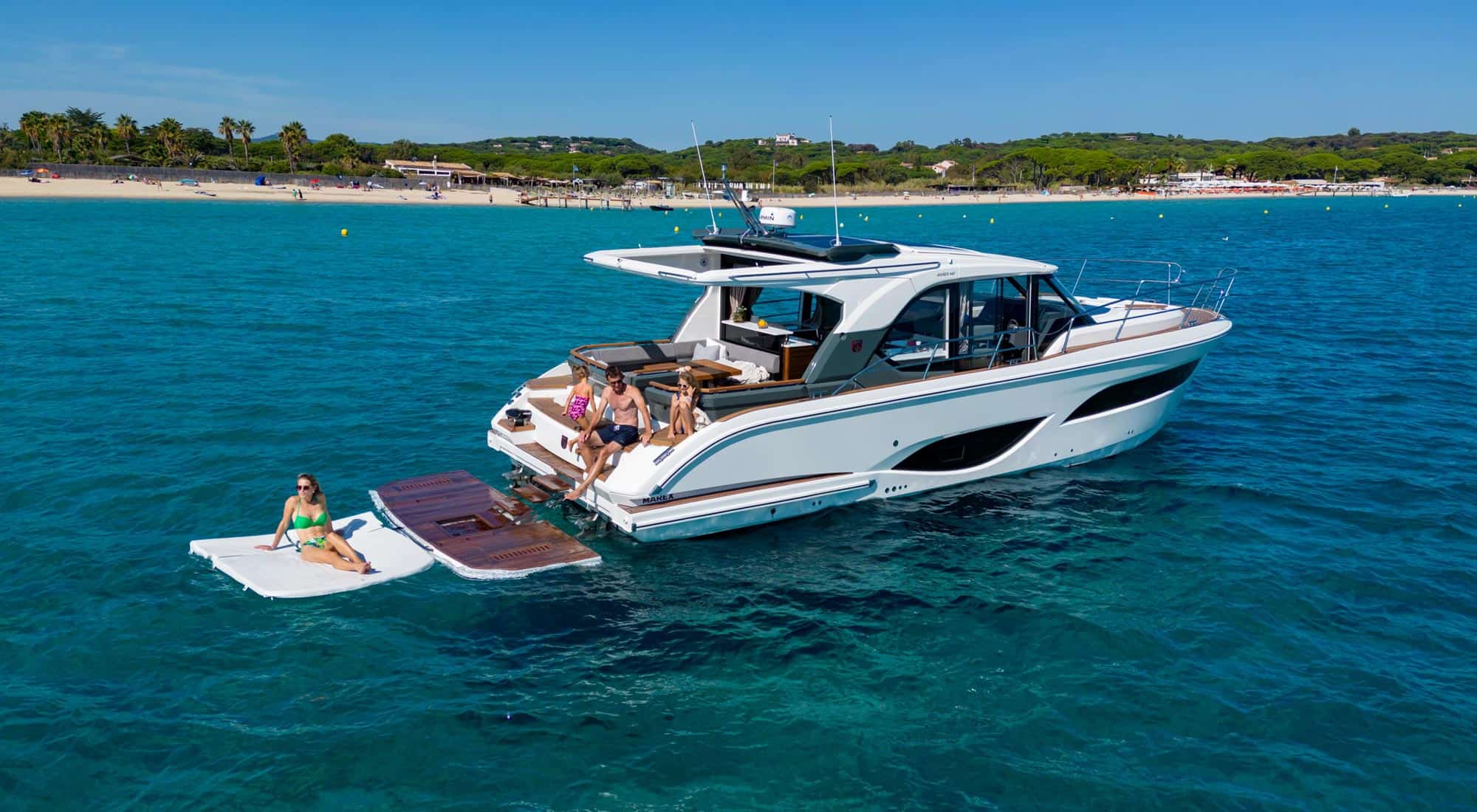 Marex 440 Gourmet Cruiser na kotwicy z ludźmi na platformie hydraulicznej i pływającej, przy piaszczystej plaży.