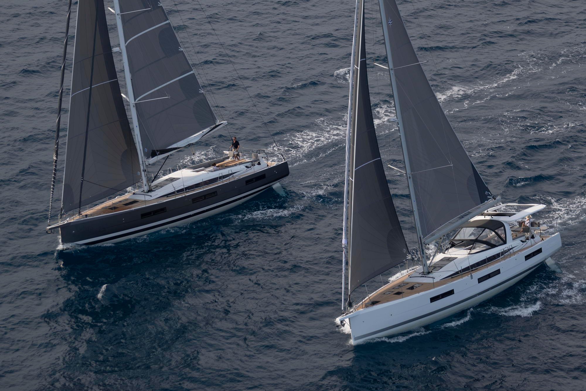 Dwa żaglowce Jeanneau Yachts 60 płynące po morzu. Jeden z ciemnym kadłubem, drugi z białym, oba z rozstawionymi żaglami.