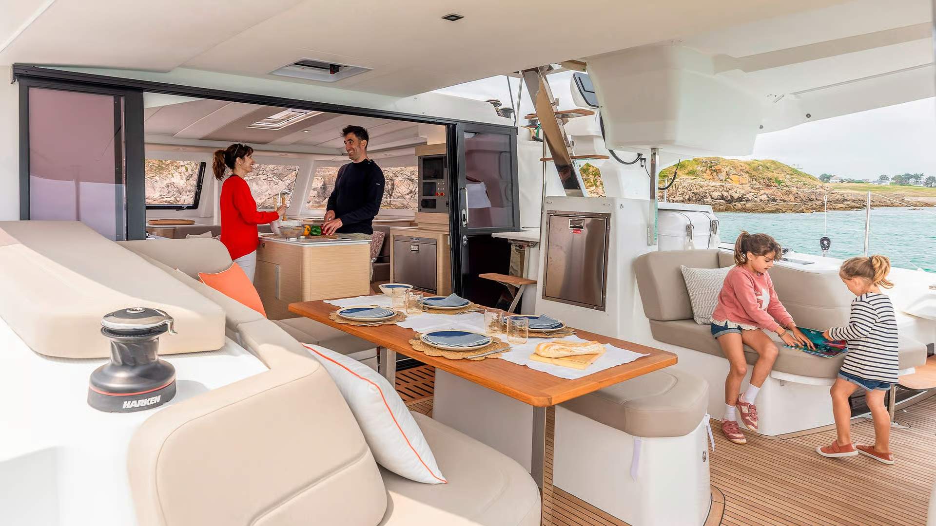 Rodzina na pokładzie katamaranu Fountaine Pajot FP41. Dorośli w kuchni, dzieci bawią się w kokpicie rufowym.